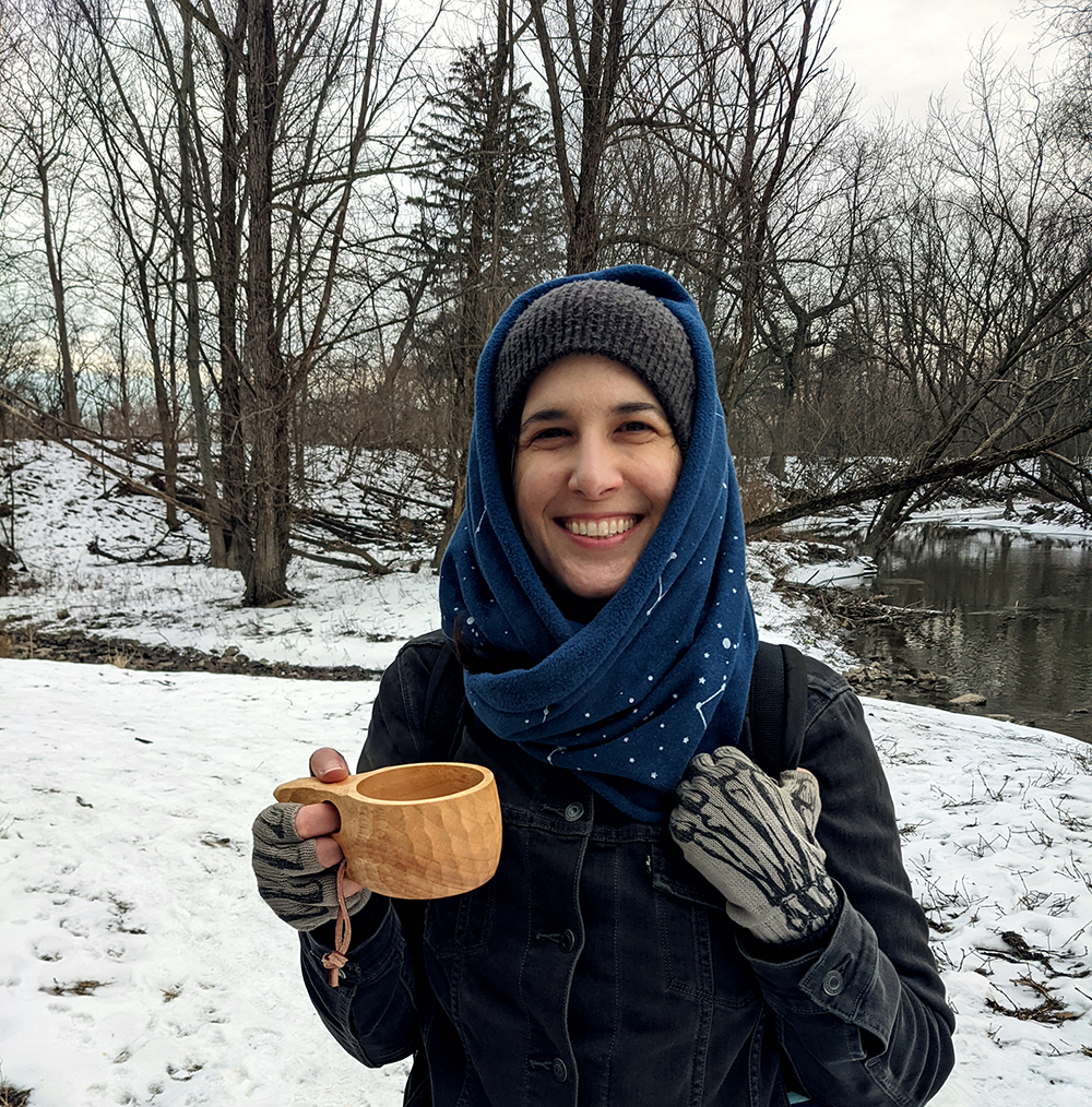 Kathy in a snowy field holding a wooden mug full of tea